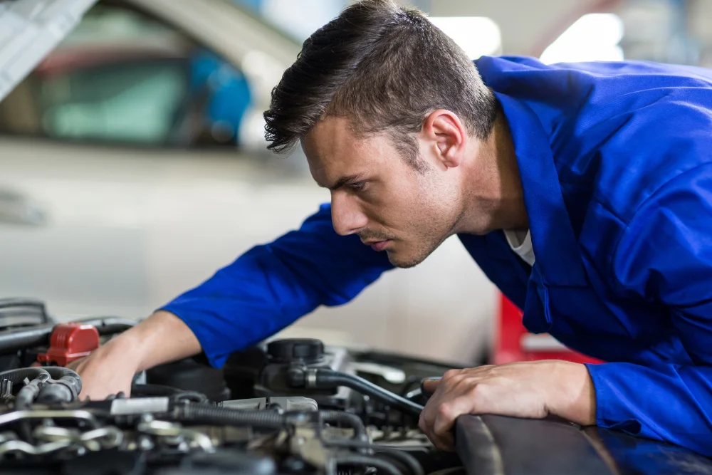 Mecânico com uniforme azul, que está debruçado sobre o motor de um carro, representando a proteção de módulo do carro da Safecar.